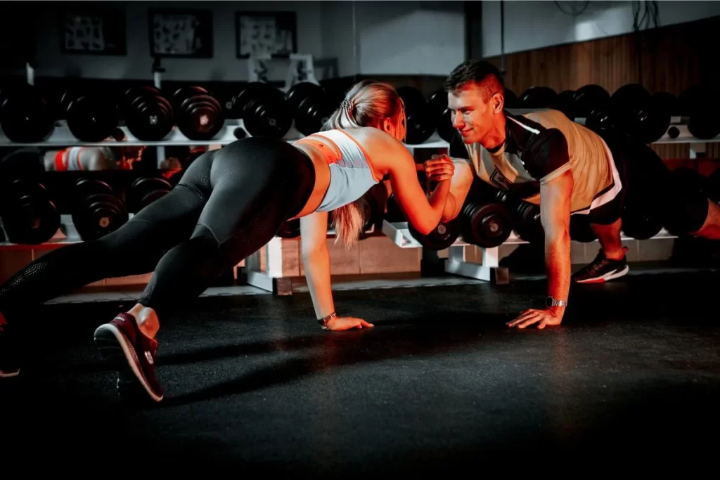 Personal trainer and client performing a plank workout exercise together in a gym environment.