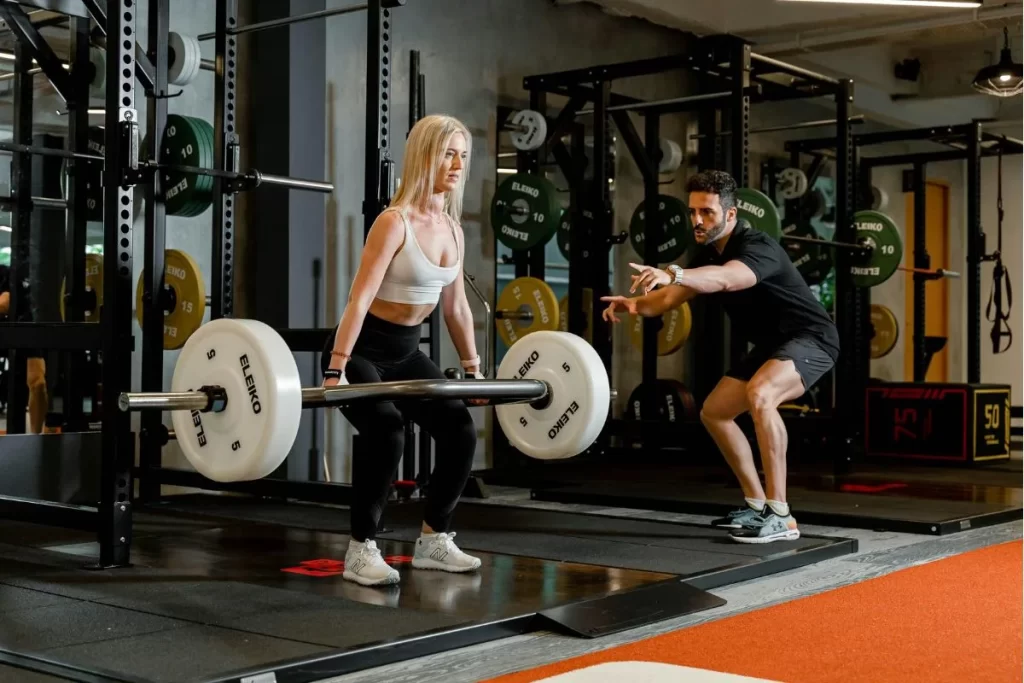 Personal trainer guiding a woman through strength training exercises in a modern gym environment.